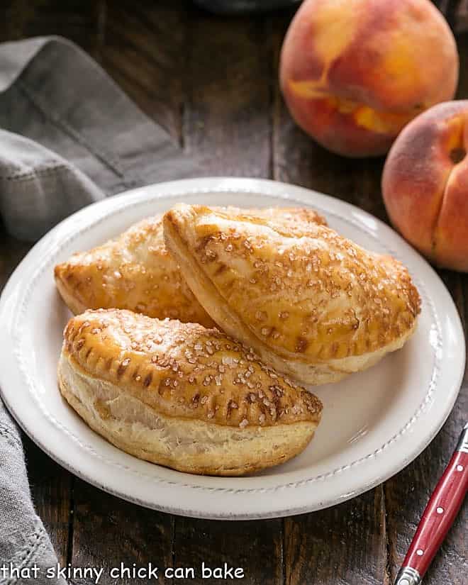Chaussons aux Pêches or Peach Turnovers - scrumptious, homemade peach hand pies Peach Hand pies on a round white plate with a red handled fork.