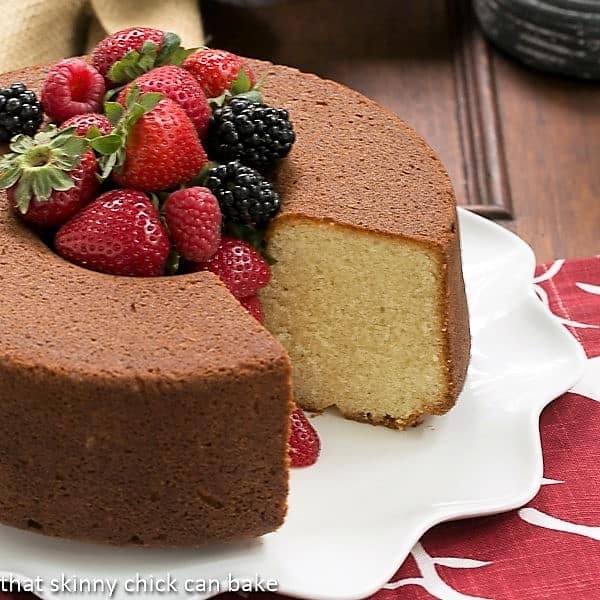 Vanilla Pound Cake - Perfect dessert topped with summer berries or any seasonal topping Whole Vanilla Pound Cake on a white platter with a slice removed and berries piled in the middle.