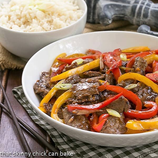Asian Beef with Peppers in a white serving bowl with a side dish of rice.