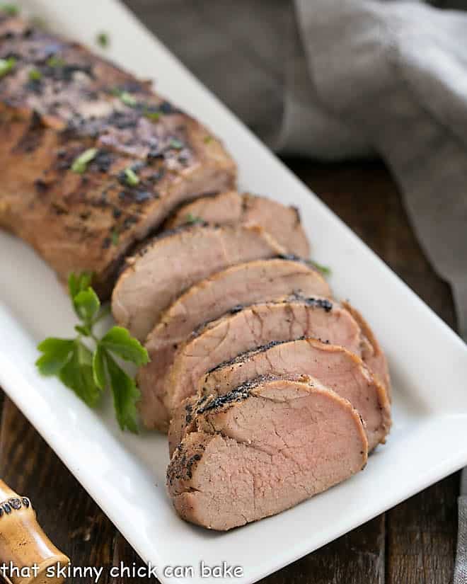 Whiskey Marinated Pork Tenderloin partially sliced on a white serving tray