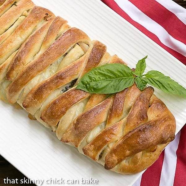 Braided Stromboli - pizza dough packed with Italian meats and cheeses Overhead view of a braided stromboli on a white platter.