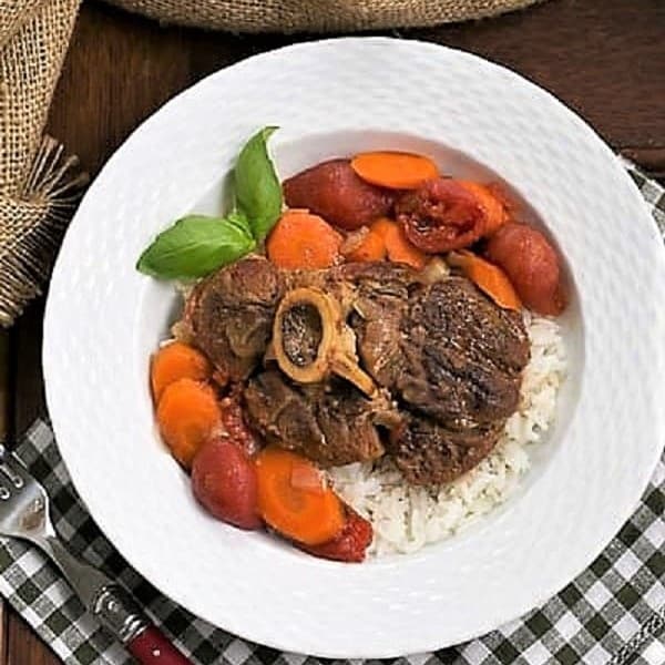 Overhead view of Osso Buco a L'arman in a white bowl over a green and white checked napkin.