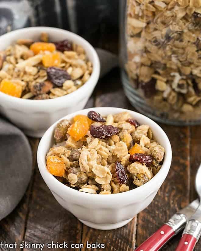 Homemade Granola iwth Pistachios, Coconut and Dried Fruit - a scrumptious combination that's perfect with milk, to top your yogurt or as a snack! Pistachio Coconut Granola in 2 white cereal bowls with 2 red handled spoons