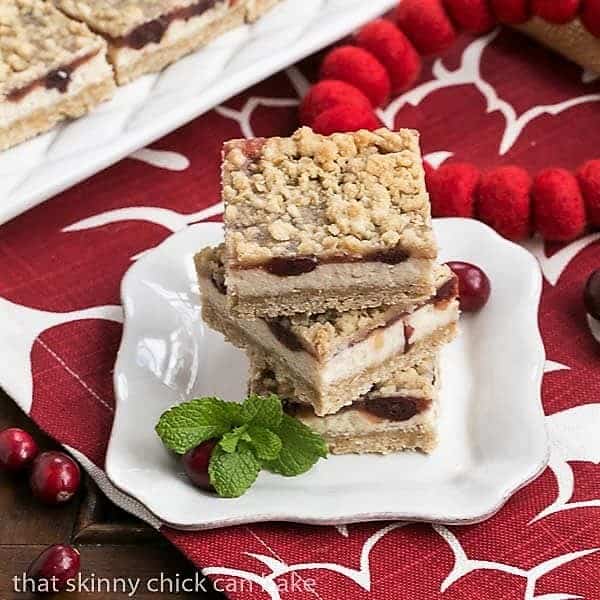 3 Cranberry Cheesecake Bars stacked on a white dessert plate.