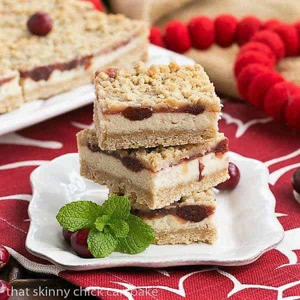 3 cranberry cream cheese bars stacked on a small white plate with a sprig of mint.