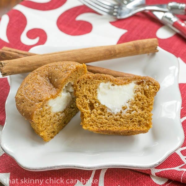 Cream Cheese Filled Pumpkin Muffin cut in half on a small white plate garnished with cinnamon sticks.