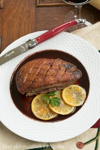 Pan Seared Duck Breasts in wine sauce on a white plate with a red handled knife.