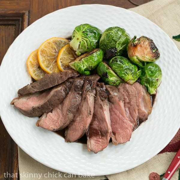 Pan Seared Duck Breasts on a plate with orange slices and Brussels sprouts.