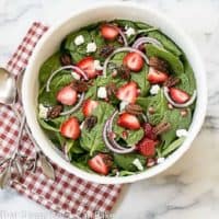 Spinach Strawberry Pomegranate Salad in a serving bowl over a red and white checked napkin