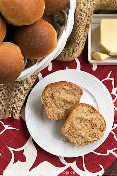 Whole Wheat Dinner Rolls in a basket and one open on a white basketweave plate.
