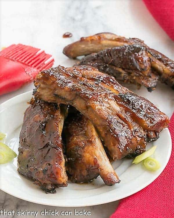 Asian Baby Back Ribs - Finger licking good with a seriously delicious glaze! Asian Baby Back Ribs on a small white plate with some thin scallion slices.