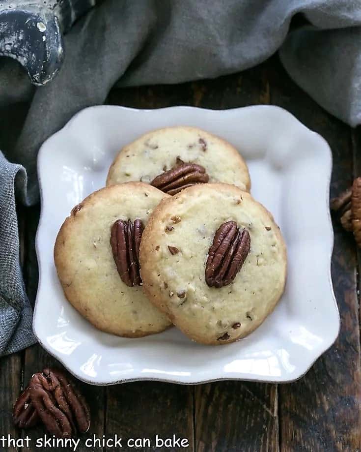 Pecan Sandies are a popular shortbread cookie, made by the Keebler company. This homemade Pecan Sandies cookie recipe is a recreation of a childhood favorite! Overhead view of 3 pecan sandies on a square white decorative plate.