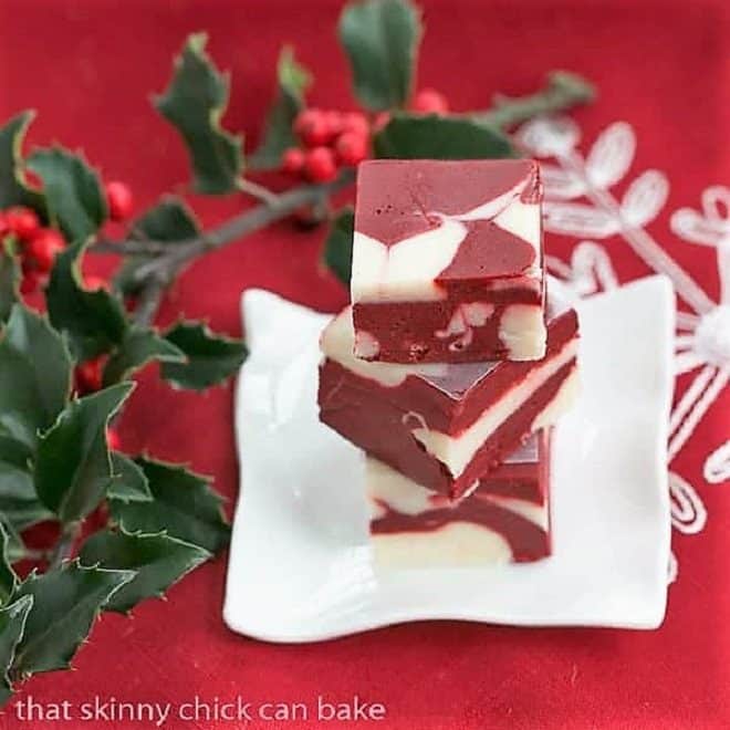 Stack of red velvet fudge on a small white plate with holly berries.