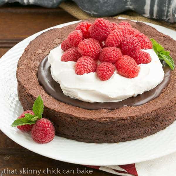 Chocolate Earthquake Cake - a dense chocolate souffle cake that is supposed to rise and fall!! Chocolate Earthquake Cake on a white plate topped with chocolate, cream and berries.