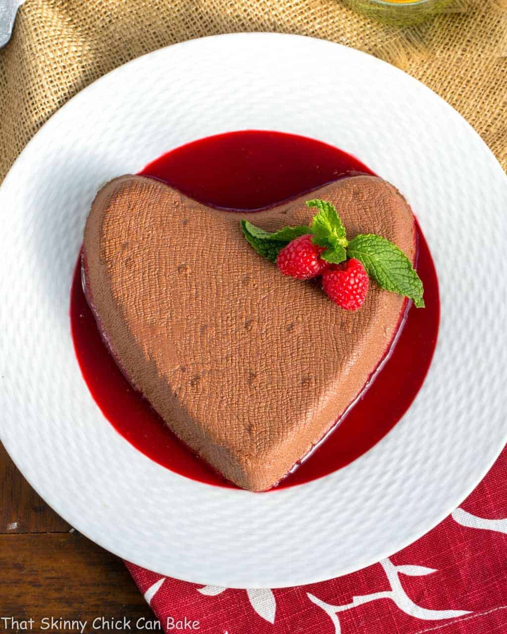 Chocolate Coeur a la Creme - This creamy heart-shaped dessert is the epitome of Valentine's Day sweets! Chocolate Coeur a la Creme on a white plate over raspberry sauce.