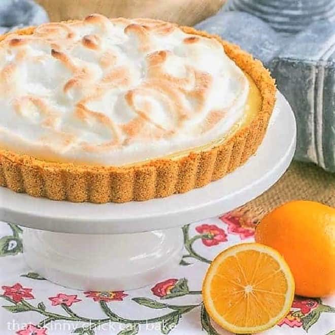 Meyer Lemon Tart with Meringue Topping on a white cake stand next to Meyer lemons.