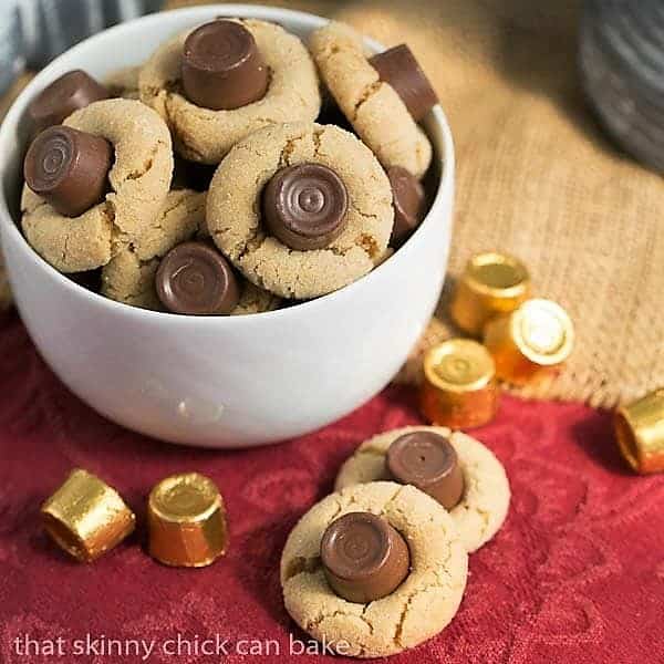 Rolo Peanut Blossoms- Sugar coated peanut butter cookies topped with a chocolate caramel Rolo Rolo Peanut Blossoms in a white bowl with two cookies on the side.
