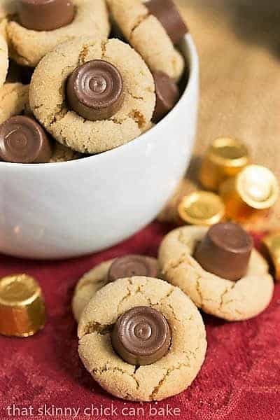 Rolo Peanut Blossoms - Sugar coated peanut butter cookies topped with a chocolate caramel Rolo Rolo Peanut Blossoms in a white bowl with a few candies and cookies on the side.