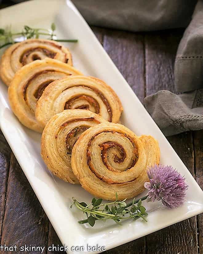 Honey Mustard Pepperoni Pinwheels - Puff pastry, mustard, Asiago and pepperoni are rolled into these irresistible pinwheels Honey Mustard Pepperoni Pinwheels on a white ceramic tray with a blossoming chive.