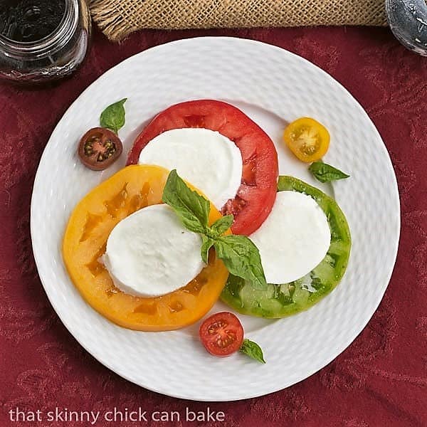 Salade de Tomates et Fromage - a simple French salad of juicy ripe tomatoes, fresh mozzarella and basil Overhead view Salade de Tomates et Fromage on a white basketweave plate