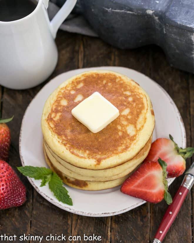 A stack of buttermilk pancakes topped with a pat of butter and served with sliced berries.