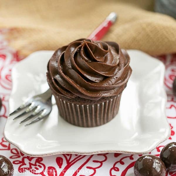 A single chocolate cupcake with a swirl of decadent chocolate buttercream on white plate with a fork.