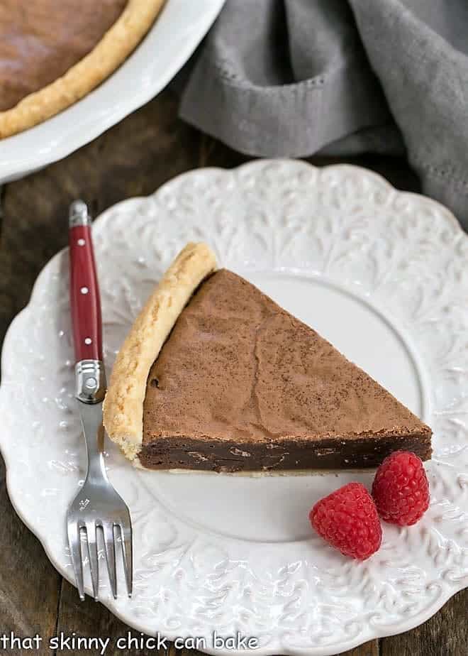 Fudgy Brownie Pie - Rich brownie filling studded with chocolate chips and baked in a flaky pastry shell! Fudgy Brownie Pie on a fancy white plate with raspberries and a red handled fork.