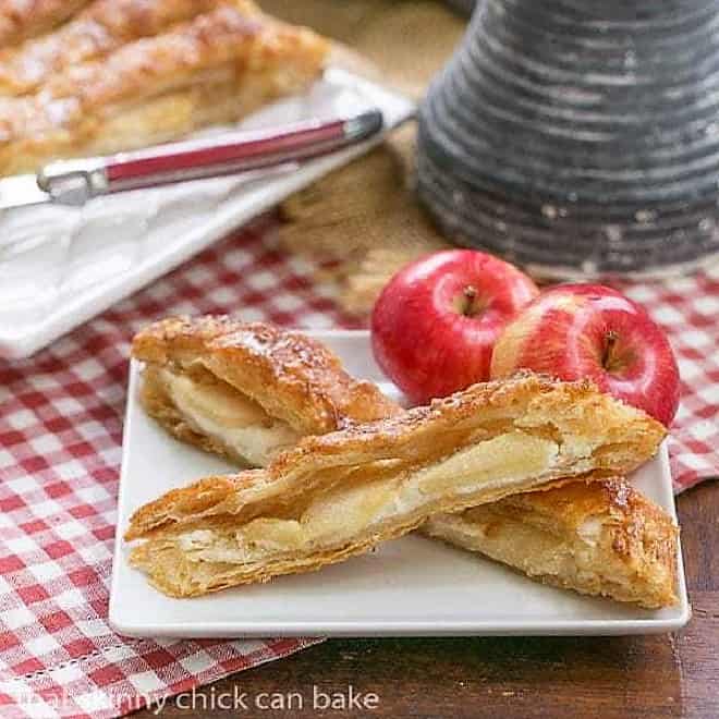 Maple Glazed Apple Tart - Puff pastry, sweetened cream cheese, apples and a maple glaze make for a spectacular breakfast or dessert 2 slices of a Maple Glazed Apple Tart on a square white plate.