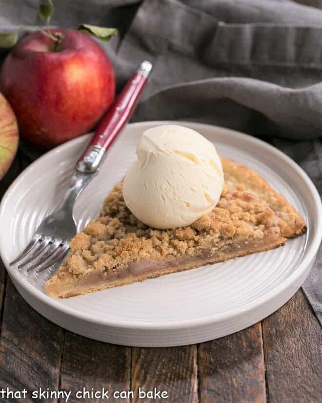 Apple Pie Pizza - A dessert pizza made with a pastry crust, spiced apples, and a crumb topping! An easy apple recipe with the taste of a Dutch Apple Pie! Apple Pie Pizza slice with a scoop of ice cream on a white dessert plate.