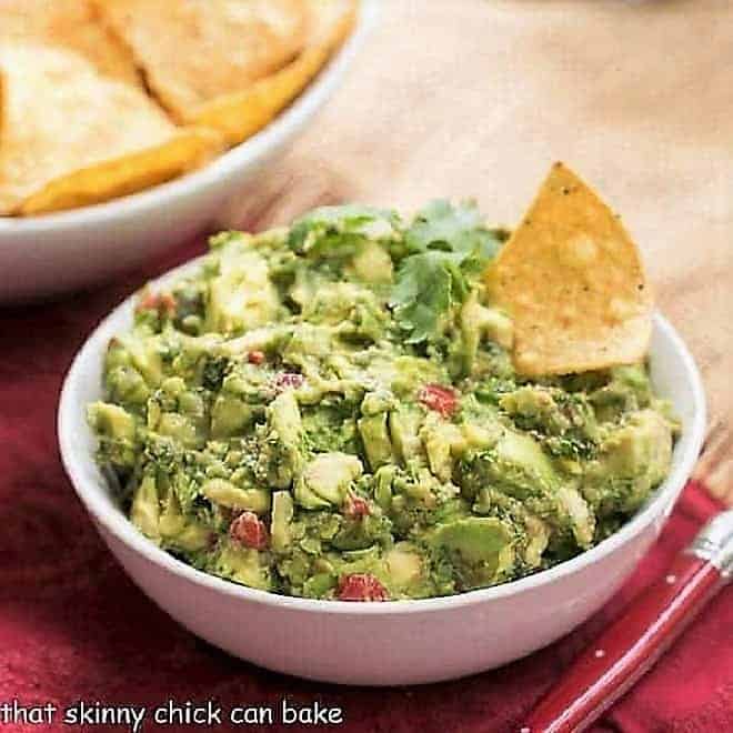 Guacamole in a white ceramic bowl with a red handled serving spoon.
