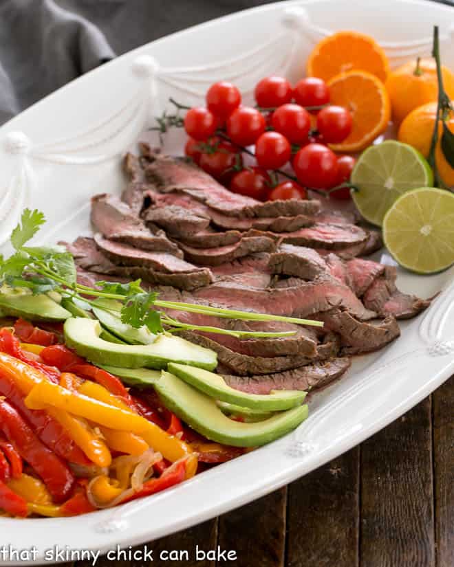 Easy Beef Fajitas - Marinated and grilled beef flank steadk wrapped in a tortilla for an easy weeknight supper Flank Steak Fajitas and toppings on a white platter.