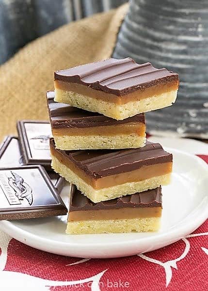 Ganache Topped Caramel Bars - Shortbread crust, caramel filling and creamy ganache topping make for one exquisite bar cookie Ganache Topped Caramel Bars stacked high on a white plate over a red and white napkin.