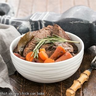 Rosemary Garlic Brisket in a white ceramic bowl and a sprig of rosemary