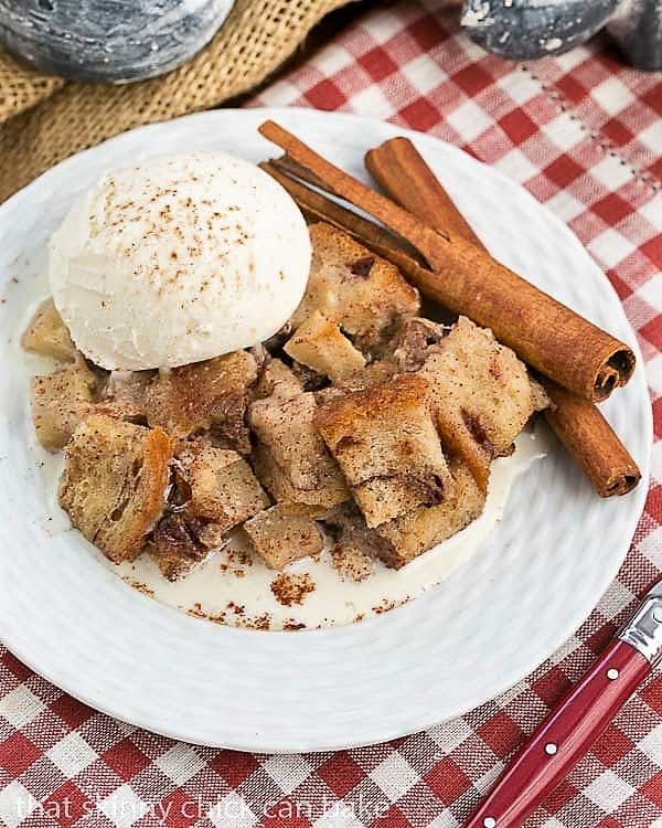 Slow Cooker Apple Pecan Bread Pudding overhead view on a white plate with ice cream and cinnamon sticks