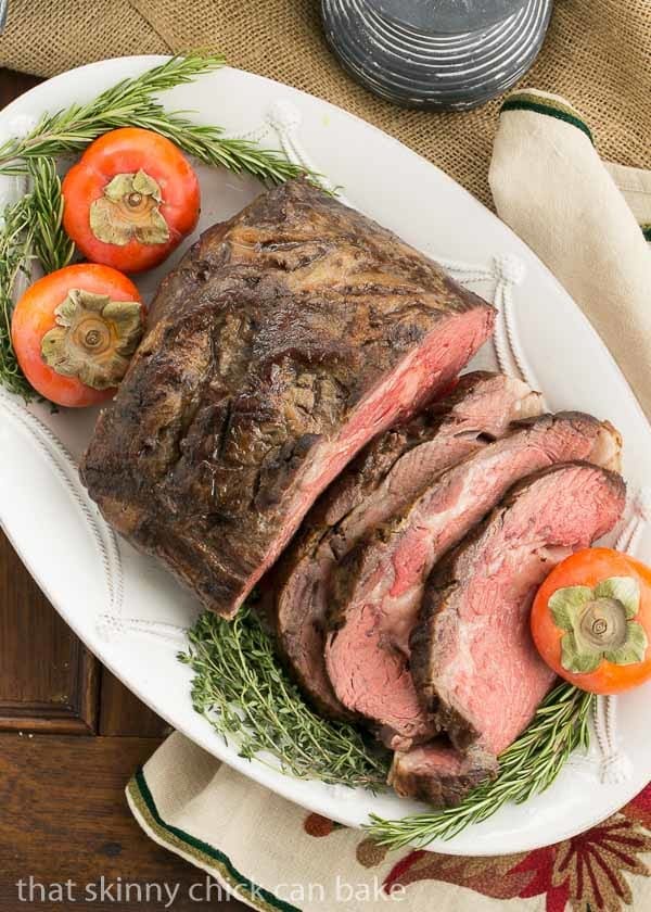 Overhead view of a Classic Prime Rib, partially sliced, garnished with fresh herbs and fruit