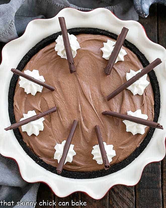 Frangelico French Silk Pie - a decadent chocolate pie topped with whipped cream and chocolate curls Frangelico French Silk Pie in a red ceramic pie plate with whipped cream and chocolate curl garnishes.