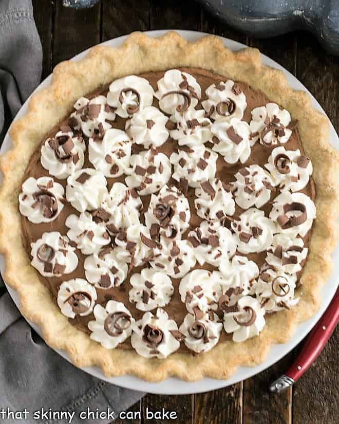 French Silk Pie with Frangelico liqueur - A decadent, luscious chocolate pie with a Frangelico twist! Overhead view of a French Silk Pie in a red ceramic pie plate with whipped cream and chocolate garnishes.