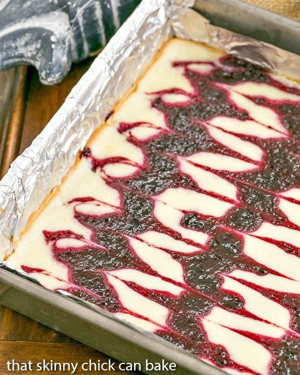 Blackberry Swirl Cheesecake Bars are sublime baked cheesecake bars with swirls of blackberry jelly. I gently swirled some homemade jelly into the batter to create these luscious Blackberry Cheesecake Bars. It's one of my favorite baked cheesecake dessert recipes. Pan of swirled Blackberry Cheesecake Bars.