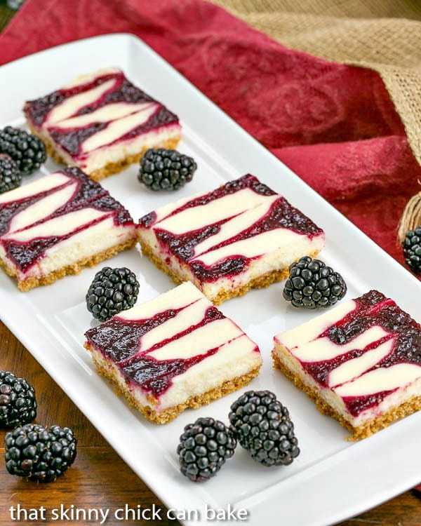 Blackberry SwirlCheesecake Bars - Sublime cheesecake bars with swirls of blackberry jelly platter of fresh blackberries and Blackberry Cheesecake Bars.