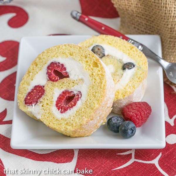 Slices of Berry Roulade on a square white plate with fresh berries to garnish.