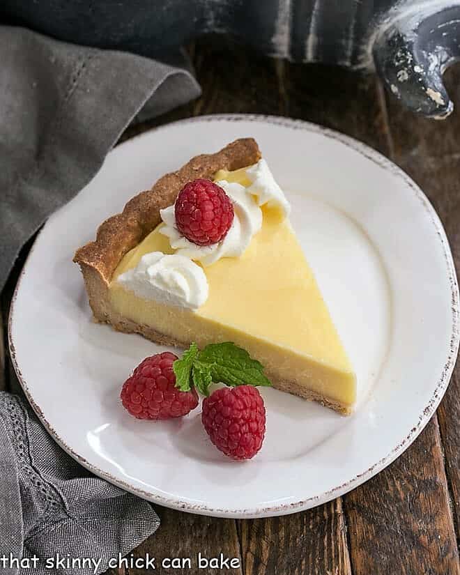 Creamy Lemon Tart - A French citrus tart that will dazzle every lemon lover! The lemon curd filling is exquisite! Slice of Creamy Lemon Tart on a white dessert plate.