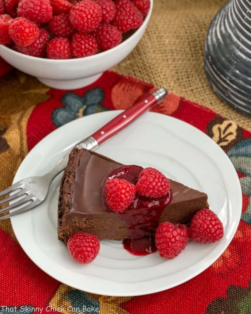 overhead image of gluten free Chocolate Torte on a white plate, garnished with chocolate ganache and raspberries