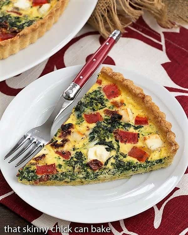 Sun-dried Tomato and Spinach Quiche - A memorable Mediterranean Quiche Sun-dried Tomato and Spinach Quiche slice on a white plate on a red and white napkin.