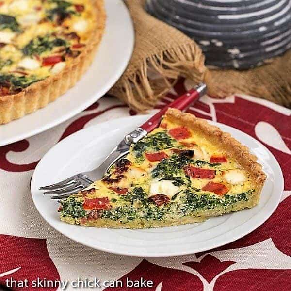 Sun-dried Tomato and Spinach Quiche - A memorable Mediterranean Quiche Sun-dried Tomato and Spinach Quiche slice on a white plate with a red handled fork.