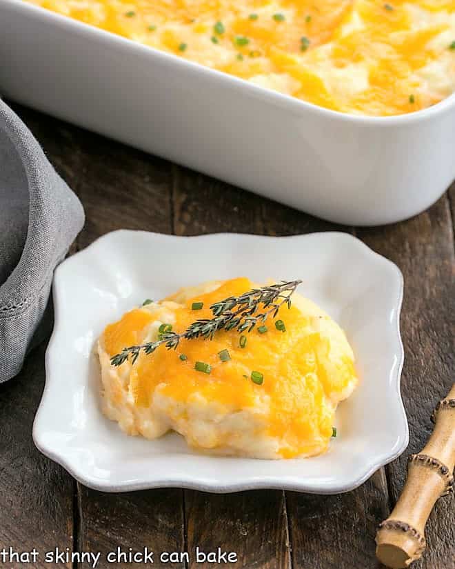 Cheesy Mashed Potato Casserole on a square plate with the casserole dish in the background