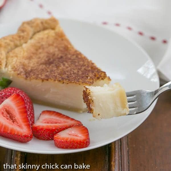 Hoosier Sugar Cream Pie -A classic dessert in Indiana made with sugar, cream and vanilla! Sugar Cream Pie bite on a fork with pie slice and strawberries on a dessert plate in the background.