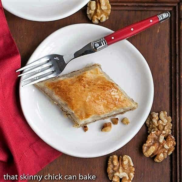 Greek Baklava Dessert - My mom's baklava with layers of buttery filo & a walnut filling doused with orange blossom water kissed sugar syrup Overhead view of a slice of Classic Greek Baklava slice on a white plate.