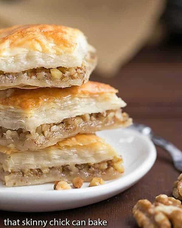 Greek Baklava Recipe - My mom's baklava with layers of buttery filo & a walnut filling doused with orange blossom water kissed sugar syrup Diamonds of Baklava Recipe stacked on a small white plate.