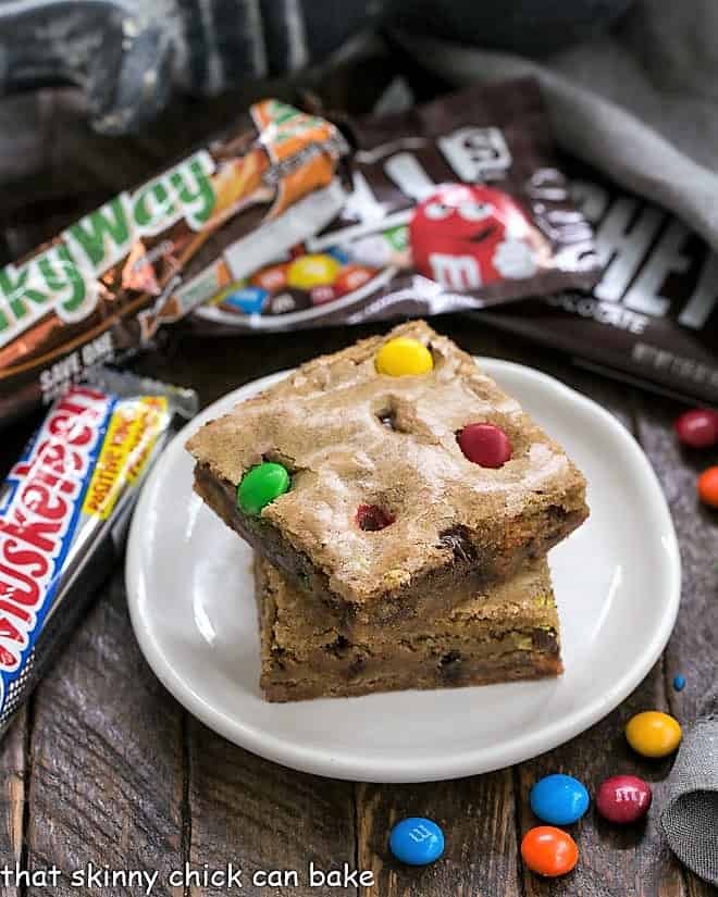 Candy Bar Blondies - The perfect way to use up any leftover Halloween candy! 2 Candy Bar Blondies stacked on a small white plate.