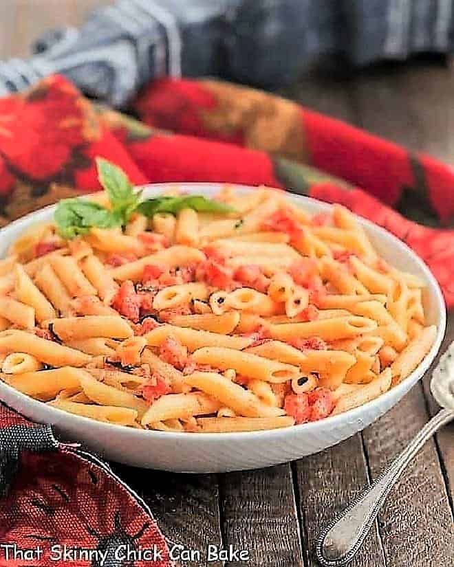 Penne alla Vodka - A simple, comforting pasta dish with tomatoes, cream and vodka! Penne alla Vodka in a white ceramic bowl with a sprig of basil.